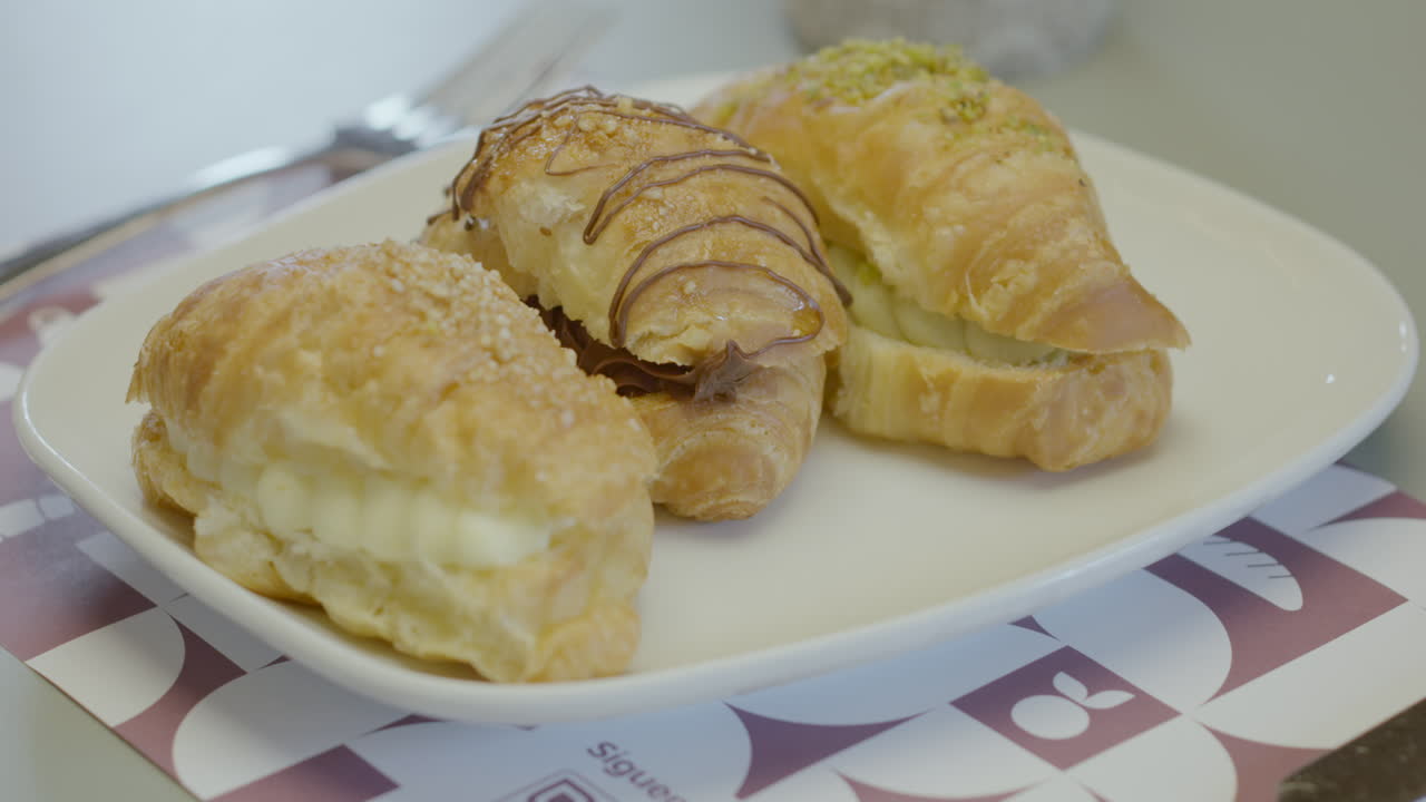 Close-up of three puff pastry croissants filled with cream, presented on a white plate