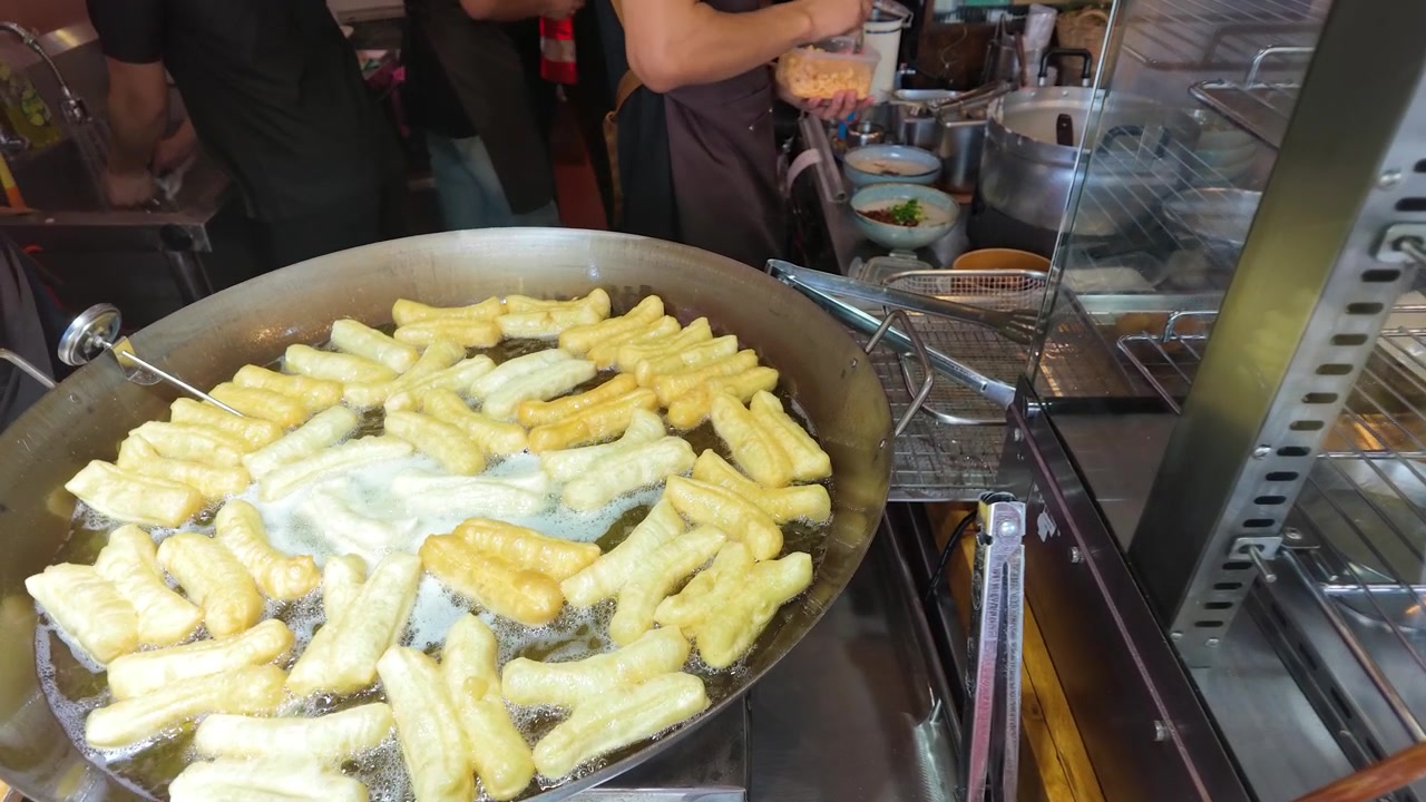 Gros plan de beignets dorés frémissant dans l'huile chaude sur un marché de rue animé.