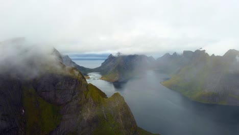 Overflight-of-the-fog-covered-mountains-in-northern-Norway-in-Lofoten-at-the-end-of-summer-towards-autumn-with-beautiful-views-over-the-fjords-and-high-steep-mountains-filmed-with-a-drone