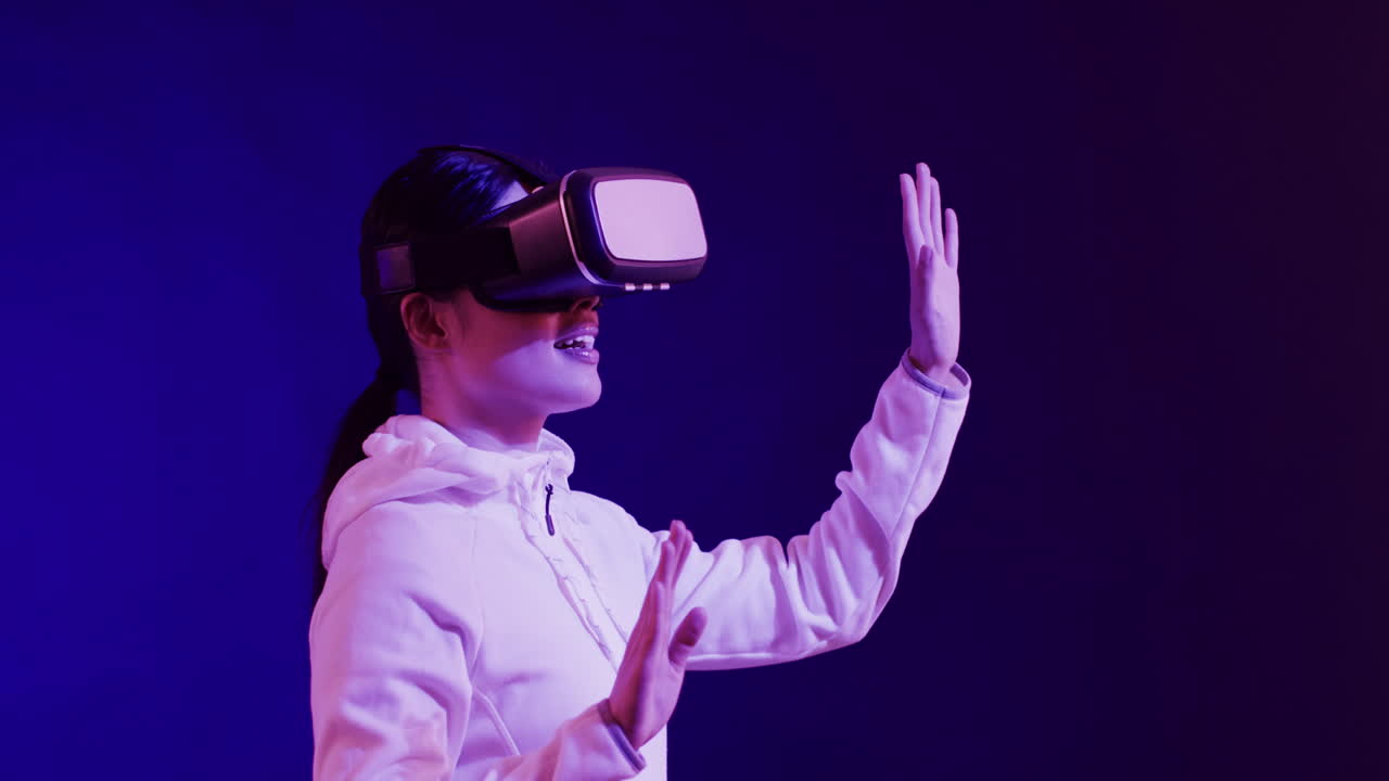 Asian woman using vr headset, touching virtual screen on blue background, slow motion