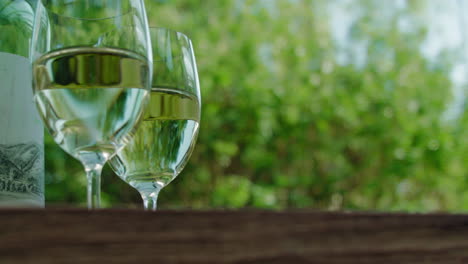 subiendo y revelando dos copas de delicioso vino blanco y una botella en una mesa de madera en el jardín en un día soleado