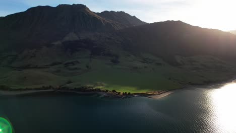 bright sun shining over mountains and lake hawea at sunrise in south island, new zealand. - aerial shot