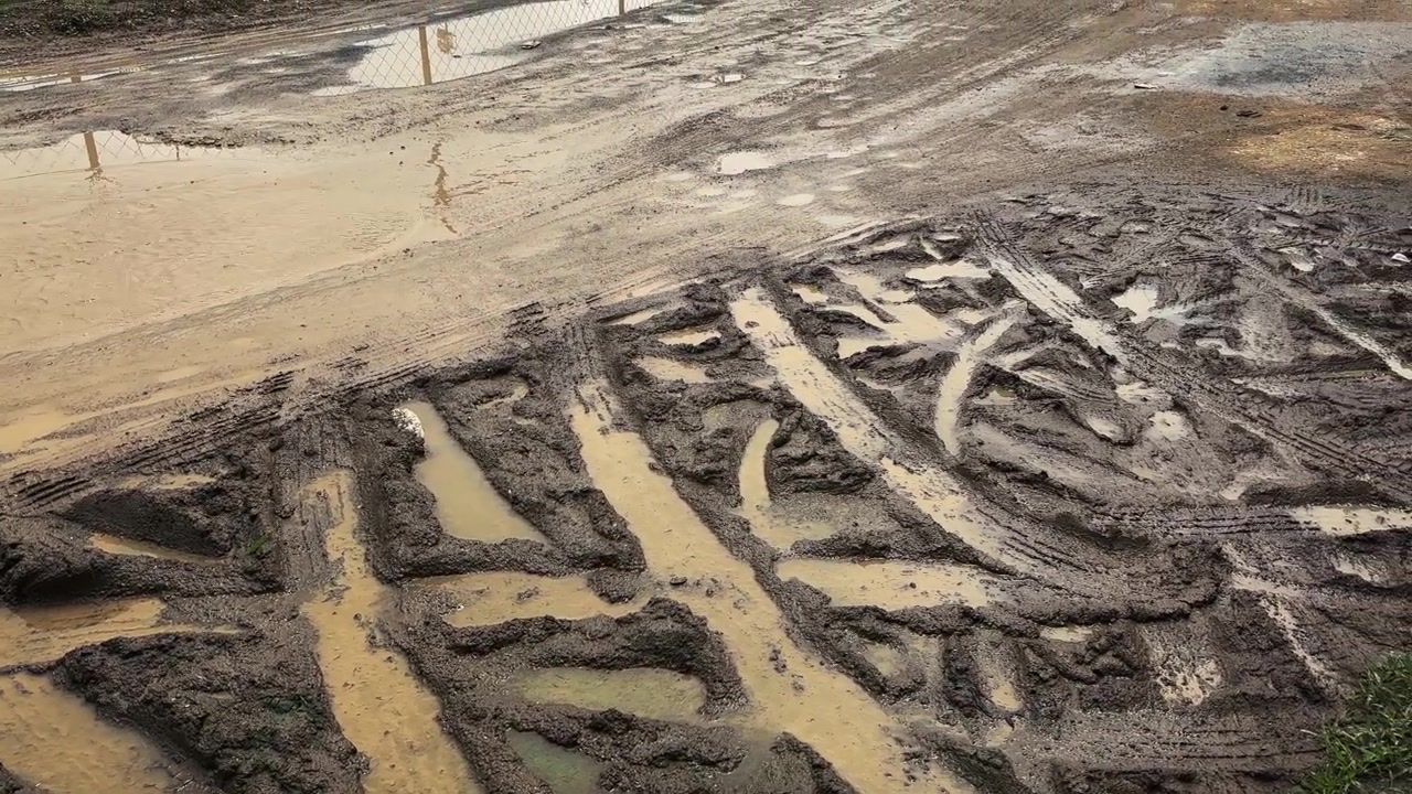 Rough dirt roadway filled with muddy ruts and rainwater puddles highlighting poor drainage and difficult travel conditions