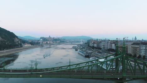 aerial drone shot of a boat on river danube in budapest at sunrise, morning, wtih liberty bridge in the foreground