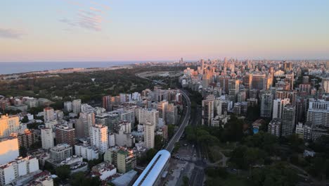 dolly in flying over a train station surrounded by buildings and parks with rio de la plata river in background, buenos aires, argentina