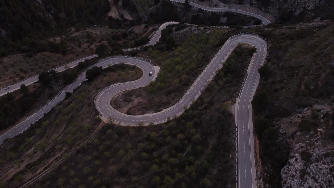 A fly over shot of a winding road in Alicante Spain, with a sole car driving slowly round a bend