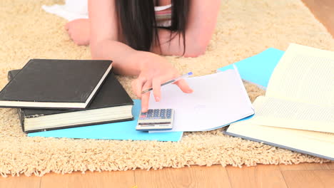 young brunette using a calculator while lying on the floor