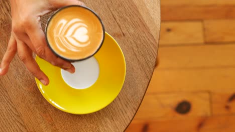 hand holding a latte art coffee cup on a wooden table