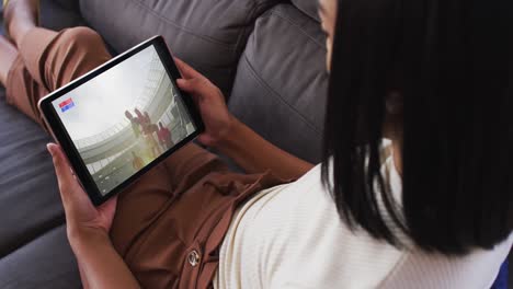 Composite-of-woman-sitting-at-home-on-couch-watching-rugby-match-on-tablet