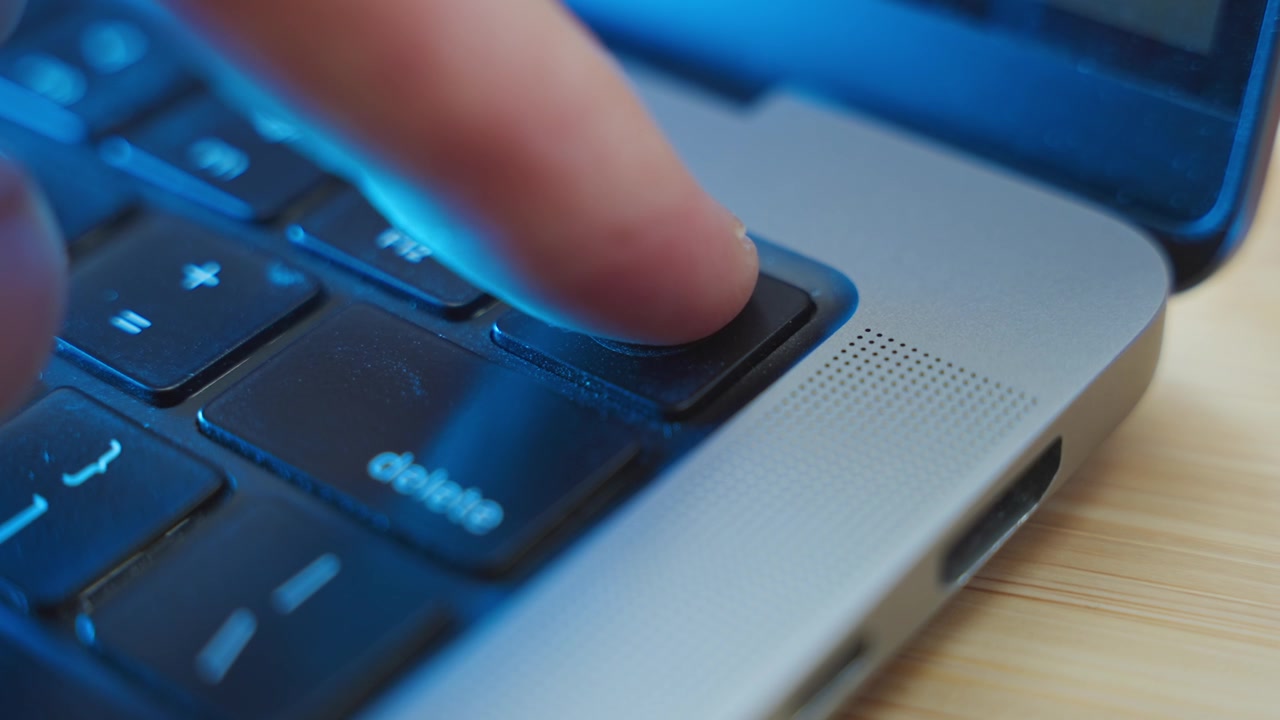 Close up on finger touching a fingerprint scanner on laptop computer at night. ID authentication approve and confirm identity by scanning fingerprint or thumbprint. Modern tech to access digital data