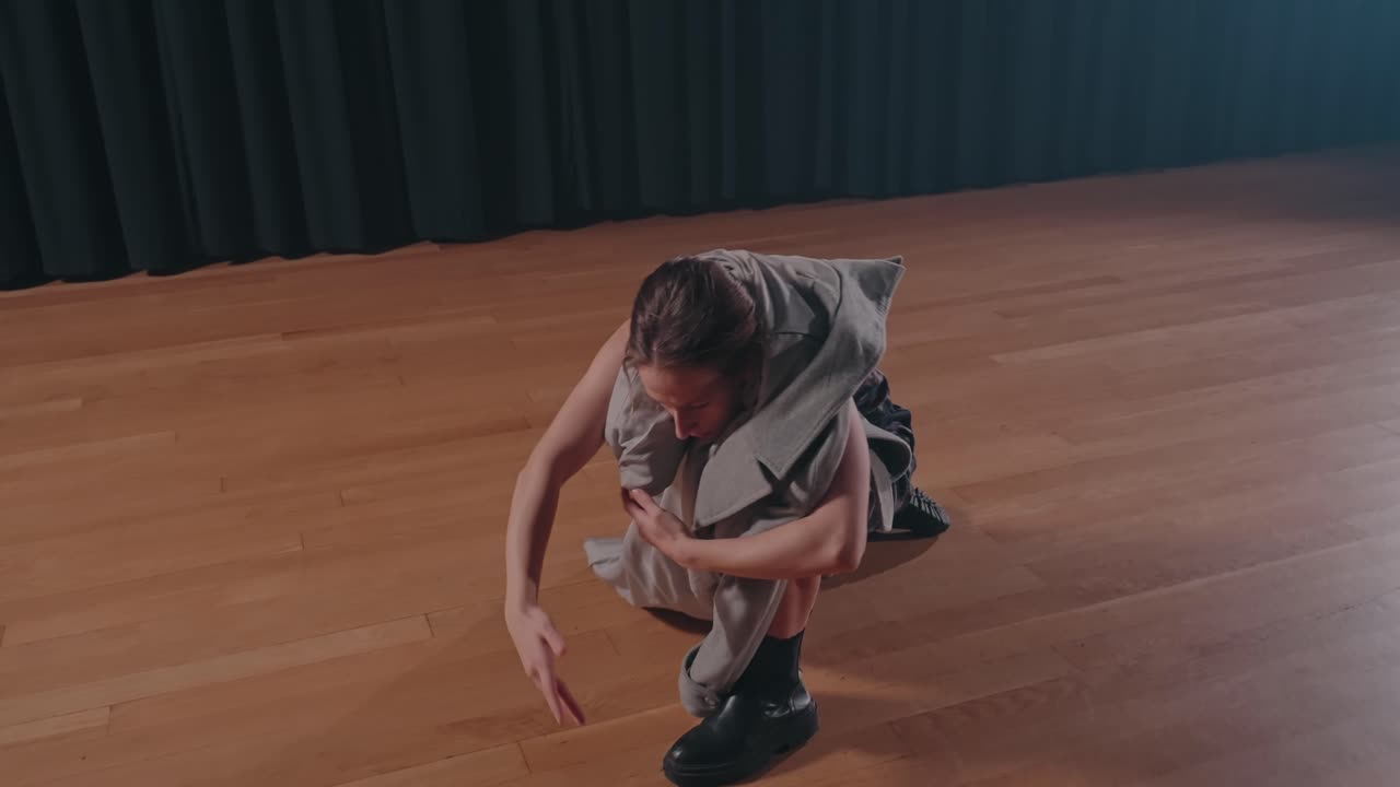 Ballerina in abito a fantasia che si muove espressivamente su un palco con pavimento in legno.
