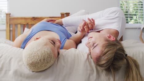 Happy-diverse-female-couple-embracing-and-lying-together-in-bed