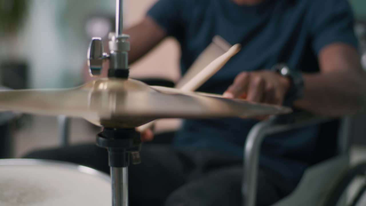 Black Male with Disability Enjoying Music and Playing Drums Rack Focus of Young African American Female with Disability Listening to Good Music in Wireless Headphones and Playing Drums during Rehearsal in Home Studio