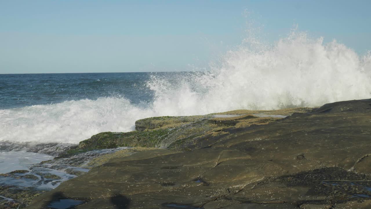 Dramatic slow-motion capture of a wave crashing against rugged rocks, showcasing splashing water and dynamic energy in mesmerizing detail.