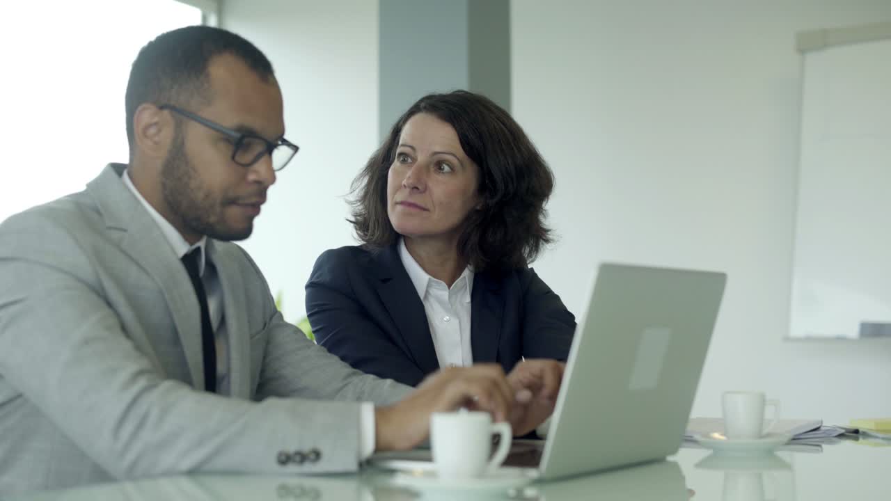 vista lateral de los empleados de la oficina sentados en la mesa y usando la computadora portátil