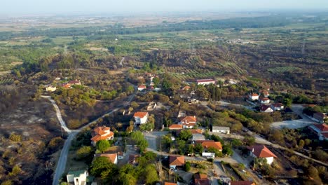 Aerial-view-of-village-surrounded-by-burnt-land-after-wildfires-in-northern-Greece,-August-2023