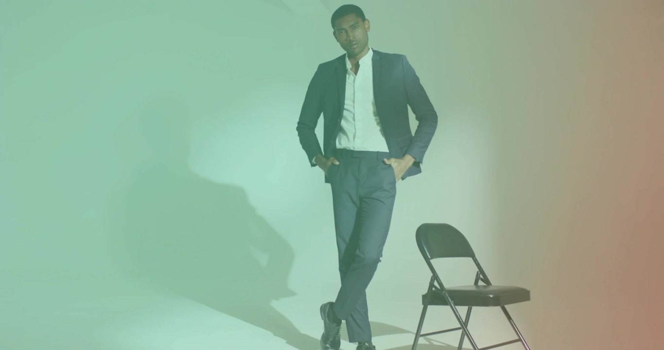 Modello maschile appoggiato a una sedia che sistema la giacca, mettendo in mostra un abito alla moda tra luci gel cangianti.
