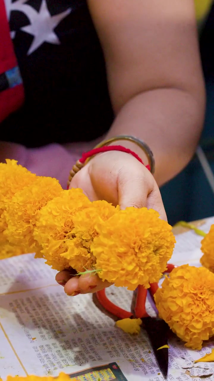 Primo piano di mani che infilano calendule gialle per creare ghirlande tradizionali al Mercato dei Fiori di Bangkok