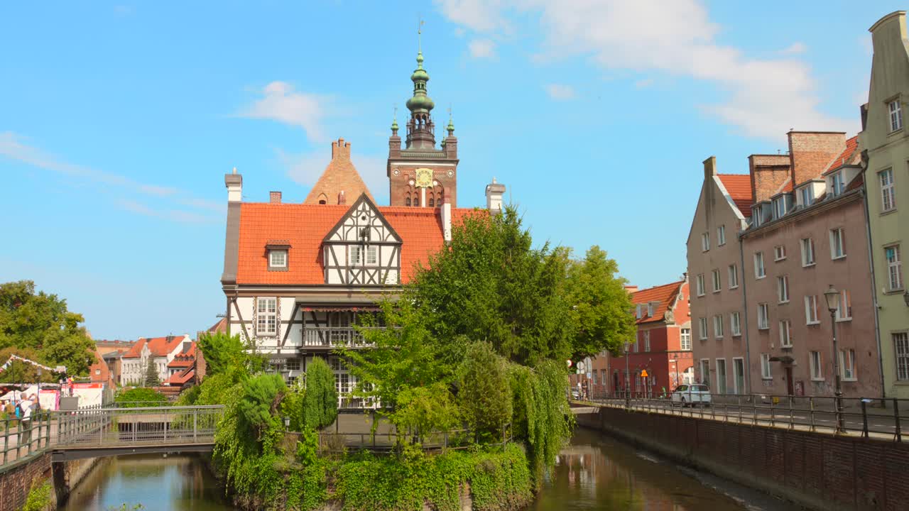 Historic buildings in Gdansk Old Town on a sunny day with trees and a canal in the foreground