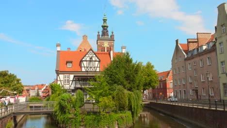 historic buildings in gdansk old town on a sunny day with trees and a canal in the foreground
