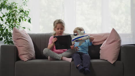 toddler plays with airplane while preschooler watches videos