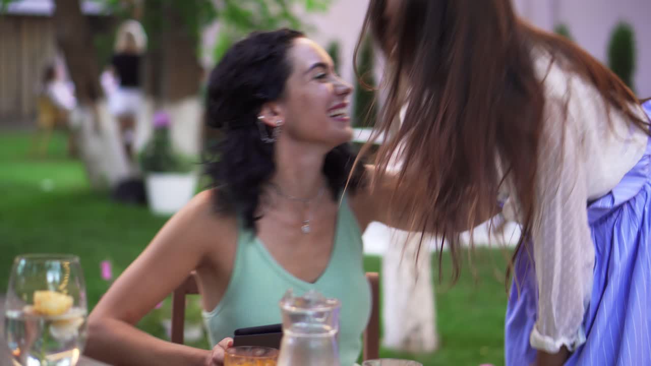 mujer morena esperando a su amiga en el café al aire libre, viene y saluda a un beso y un abrazo