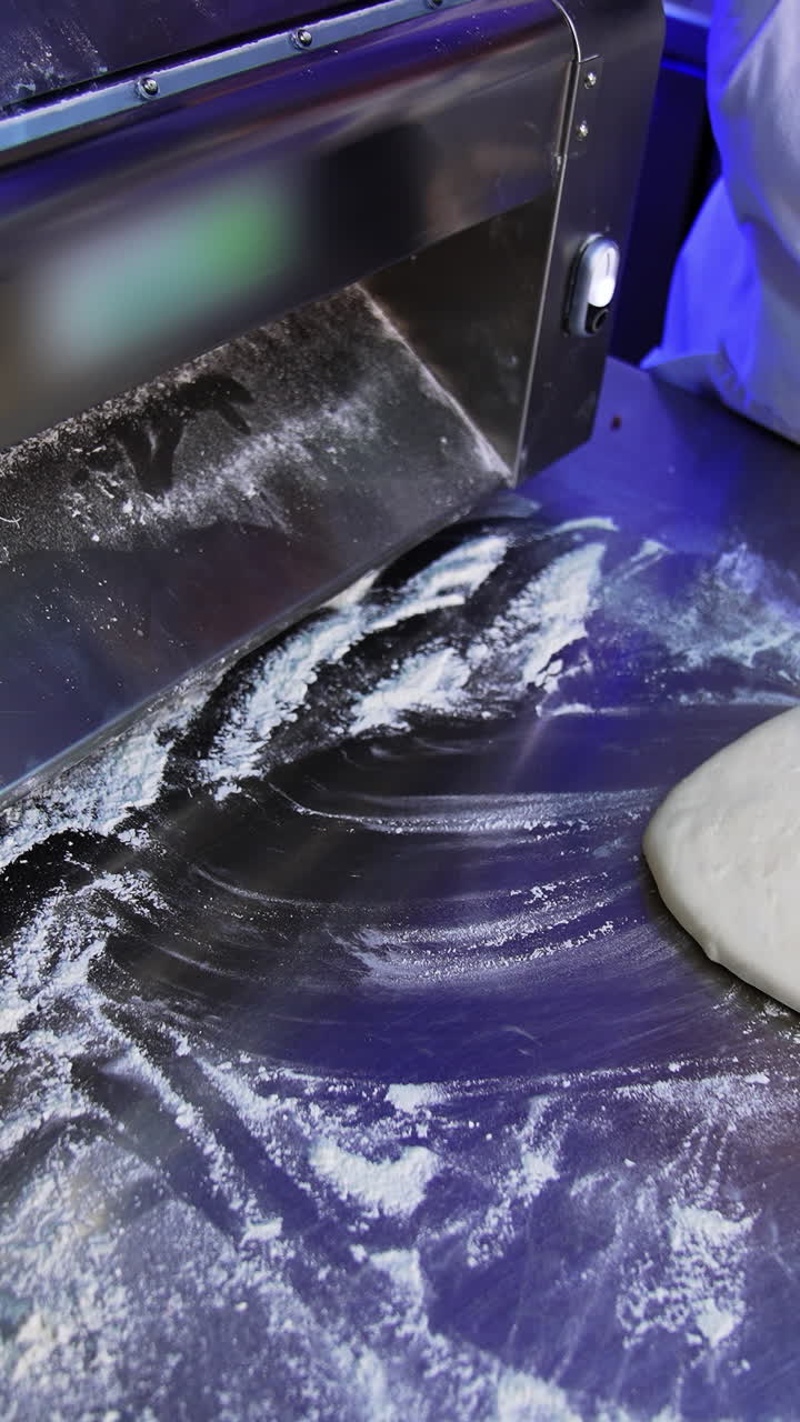 Sheeter machine for flattening dough at ravioli production. Hands of food factory worker pull the pastry from a roller machine. Vertical video