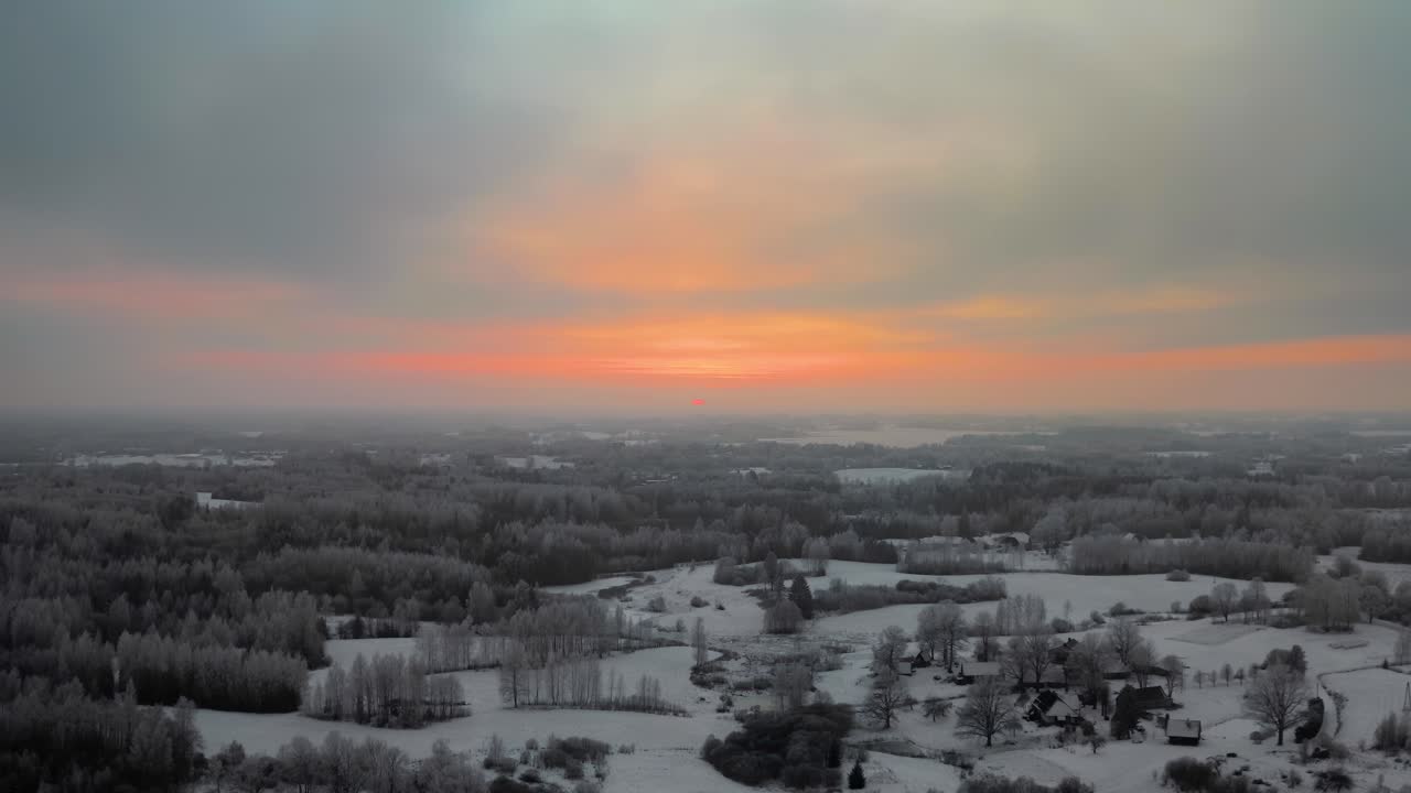 Aerial drone view of a stunning frozen forest at sunset. Breathtaking winter landscape with snow-covered trees in the countryside with vibrant, colorful and cold winter evening.