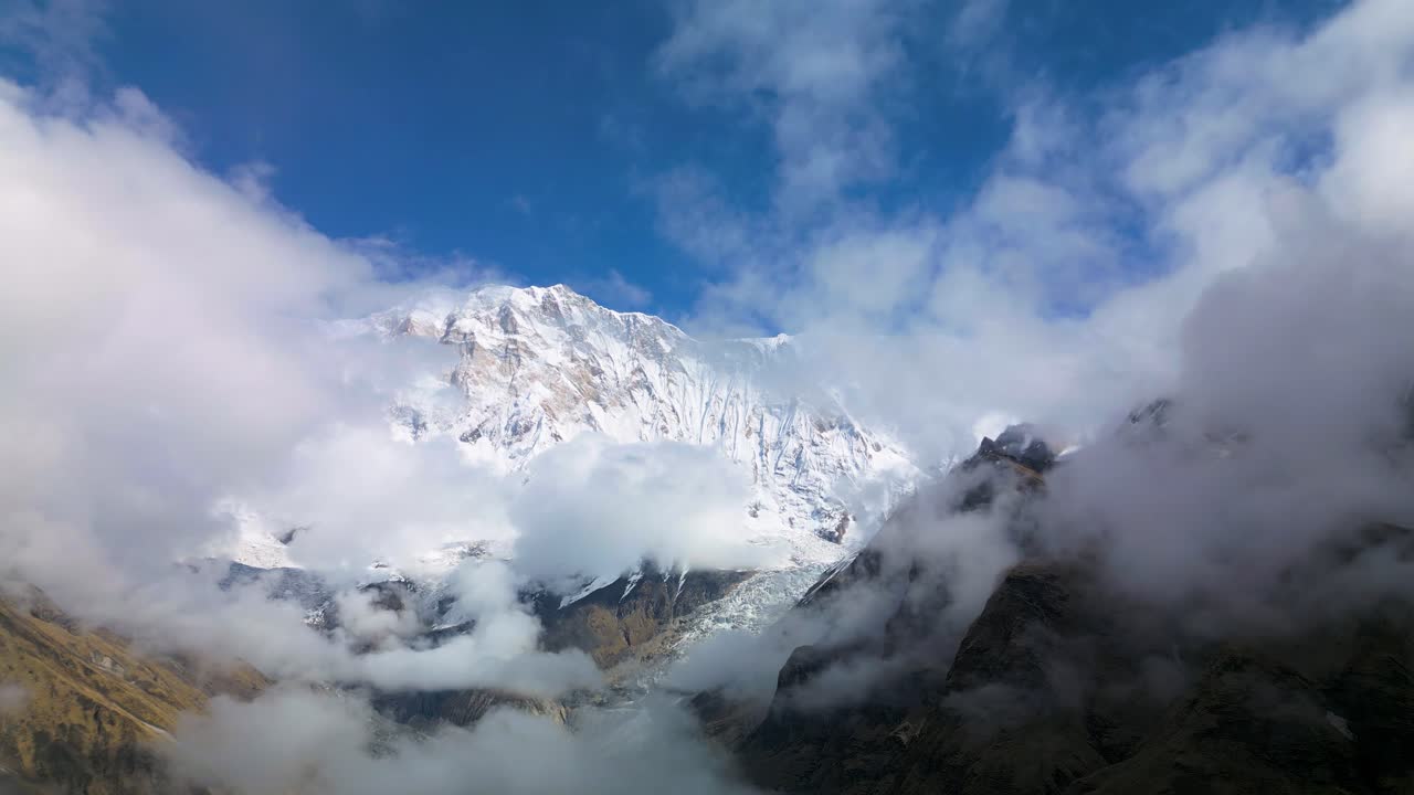 Majestic view of Mount Machhapuchhre in Nepal with its snow-covered peak emerging through drifting clouds under a clear blue sky, capturing the grandeur and serenity of the Himalayas
