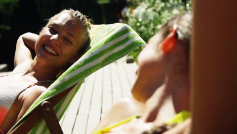 two womens interacting with each other while sunbathing near swimming pool