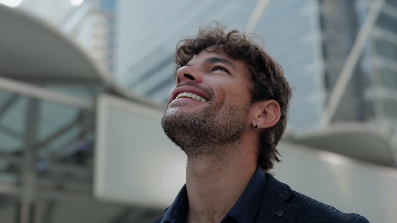 Giovane uomo felice che guarda in alto e sorride in una città moderna