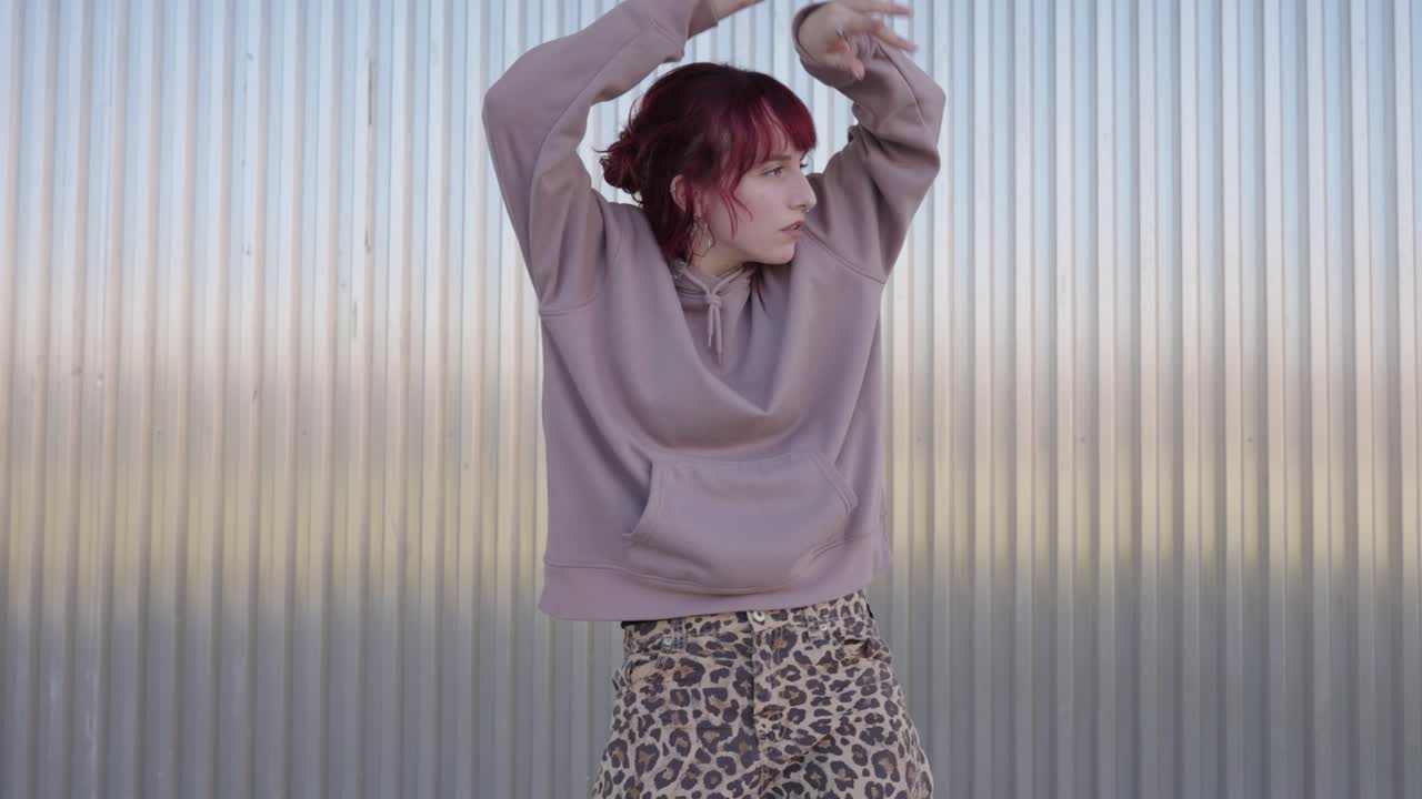 Young redhead dancer performing modern choreography against metal wall
