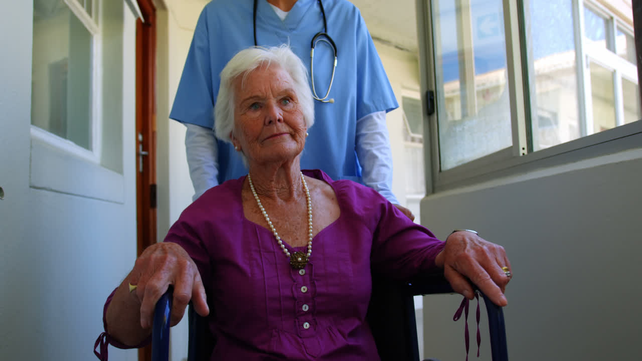 vista frontal de una doctora caucásica empujando a un paciente anciano en silla de ruedas en un hogar de ancianos 4k