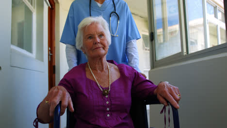 Front-view-of-Caucasian-female-doctor-pushing-senior-patient-in-wheelchair-at-nursing-home-4k