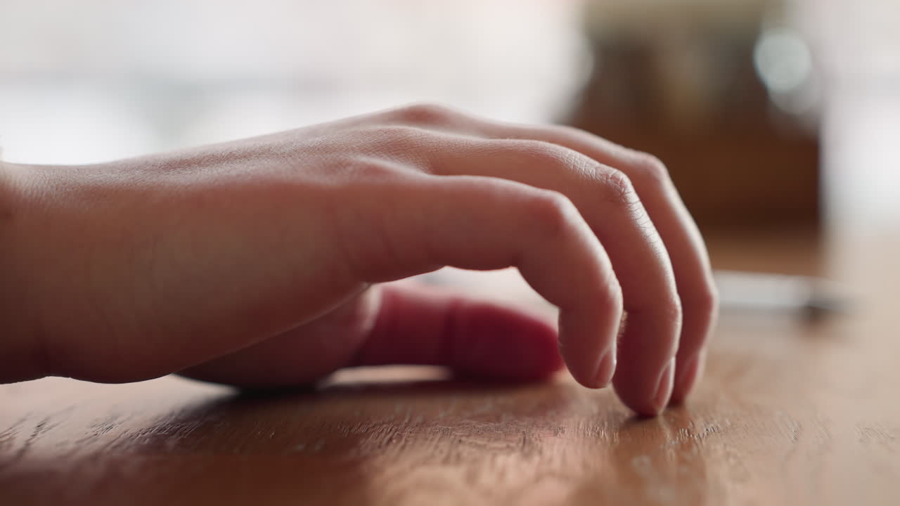 Close up side view of hand in white sleeve gently tapping wooden table with finger in soft natural lighting and blurred background suggesting calm mood, thoughtful moment