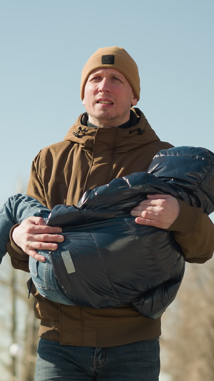 길을 는 동안 아이를 들고 있는 아버지의 클로즈업, 피곤해 보이는 아버지, 갈색 재과 베니를 입고, 아이는 검은색 부풀어있는 재을 입고 있습니다.