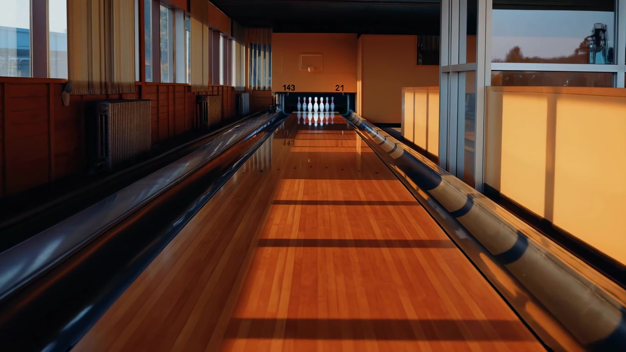 Tom inomhus bowlinghall med polerad träbana som leder mot stående käglor, varmt solljus strömmar in genom höga sidofönster, långa skuggor sträcker sig över den glansiga ytan, centrerad lågt.