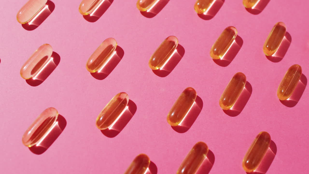 vídeo de cápsulas de aceite dispuestas en filas sobre un fondo rosado.