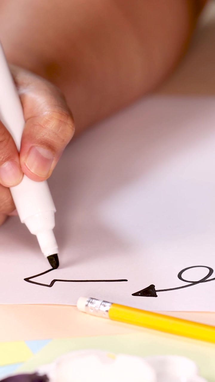 A person uses a black marker to draw directional arrows on paper, vertical composition.