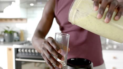 sección media de un hombre afroamericano preparando un batido saludable en la cocina en casa, cámara lenta