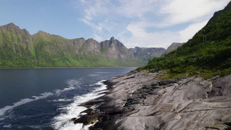 flying parallel to rocky beach at bay with mountainrange in background in norway on the island senja