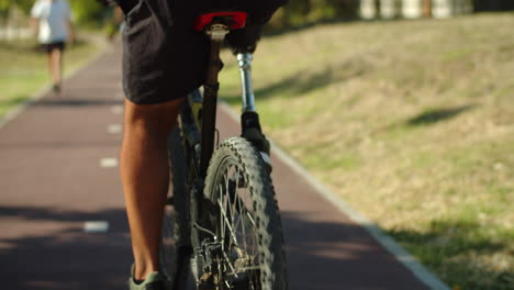 Back-view-of-man-with-artificial-leg-cycling-along-greenway