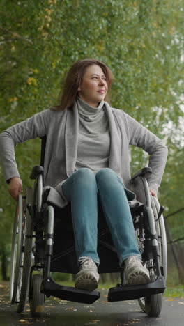 mujer con lesión se mueve girando las ruedas de la silla de ruedas con las manos. sonrisas femeninas positivas observando la naturaleza alrededor. recreación en el parque tiro de bajo ángulo