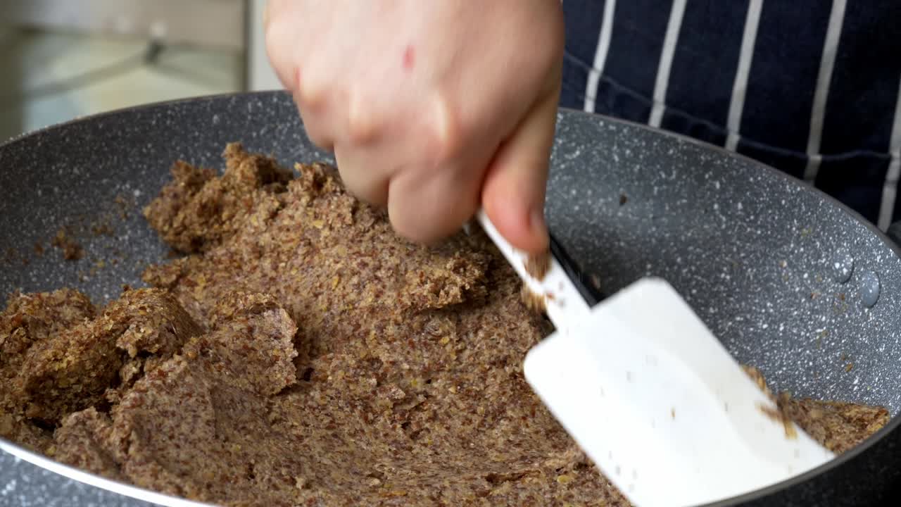 Chef spreads a flaxseed dough mixture in a skillet with a silicone spatula