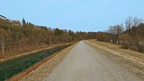 バイエルン州南部の砂道で、流れる川の隣の田園風景で自転車に乗っているドライバーからの眺め