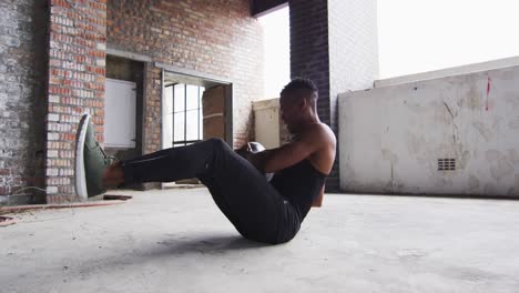 hombre afroamericano haciendo ejercicio con una pelota de medicina en un edificio urbano vacío