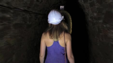 Girl-walking-in-a-mine-tunnel,-wearing-a-security-helmet,-Montevecchio,-Sardaigna