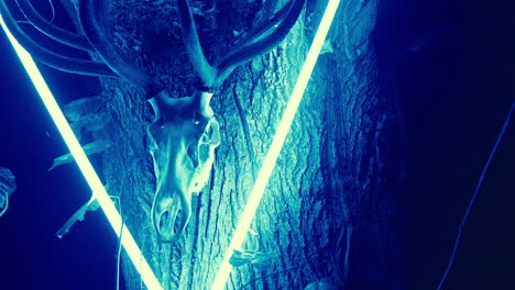 deer skull decorated with neon lights on a tree trunk at night