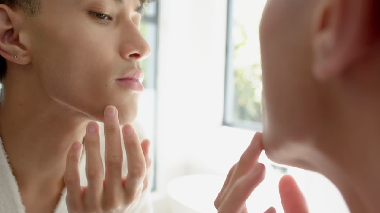 Looking in mirror, person examining face and touching chin at home