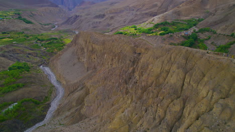 Drohnenaufnahme-Von-Wüstenhügeln-In-Mustang-Nepal,-Wo-Der-Fluss-An-Hügeln-Vorbeifließt,-Die-Von-Grüner-Vegetation-Umgeben-Sind